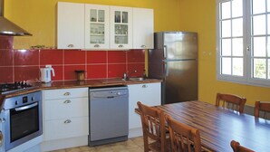 Une cuisine compacte équipée d’une cuisinière, d’un four, d’un lave-vaisselle et d’un réfrigérateur. On y trouve une table à manger avec des chaises, ainsi qu’une fenêtre qui laisse entrer la lumière naturelle.