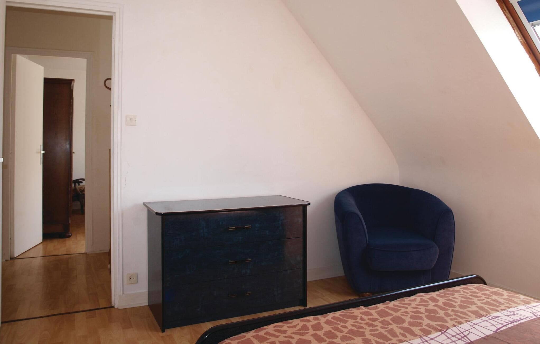 Una habitación con un aparador de madera oscura, una silla azul y una cama con colcha estampada.