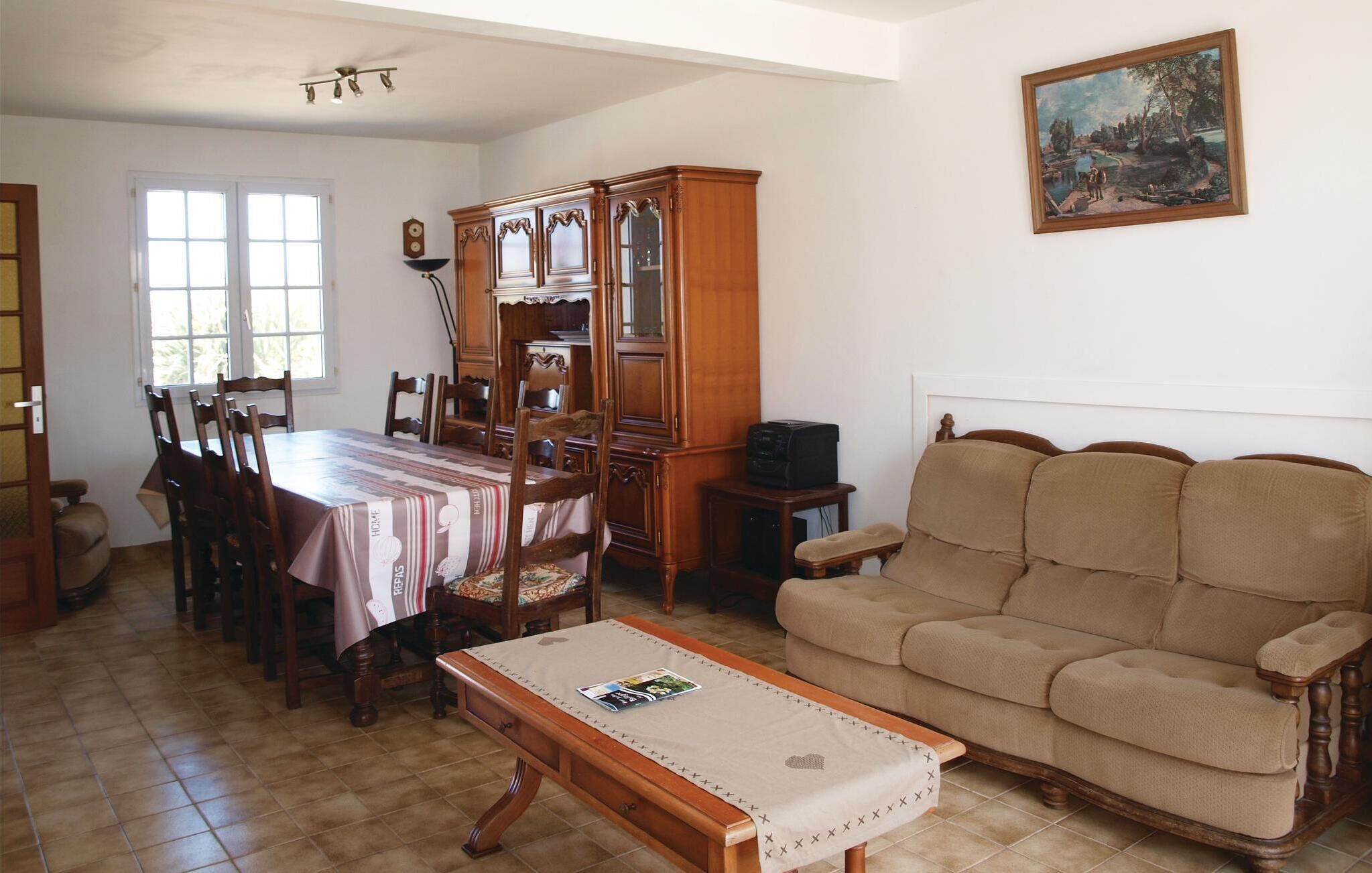 A dining area with a wooden table and chairs, a wooden cabinet, a beige sofa, and a painting on the wall.