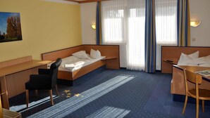 Habitación de hotel con cama, escritorio, silla y ventana con cortinas.