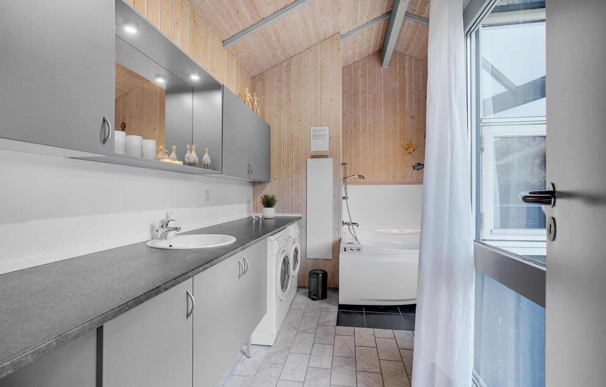 A modern bathroom with a grey sink, a mirror, a shower, and a window.