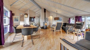 Un vaste espace de vie doté d’un plafond en bois, d’une cheminée centrale, d’une table à manger avec des chaises, d’un canapé et d’un téléviseur fixé au mur.