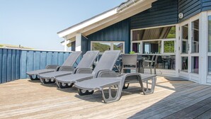 Une terrasse extérieure couverte, dotée de quatre chaises longues et d’une table, offrant une vue panoramique.