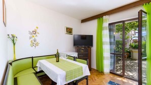 A cozy room with a dining table, green cushioned seating, a flat-screen TV, and a sliding glass door leading to an outdoor area. - Holiday apartment with terrace (Crikvenica)