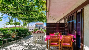A covered outdoor patio with a table and chairs, a bench, and potted plants. - Holiday apartment with terrace (Crikvenica)