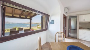 Ein Zimmer mit Meerblick, einem Esstisch, Stühlen, einer Küchenzeile mit Kühlschrank und einem kleinen, blauen Pool.