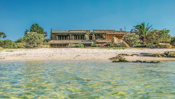 Ein Küstenanwesen mit klarem Wasser, einem Sandstrand und üppiger Vegetation.