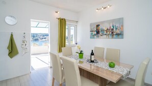 Ein Essbereich mit einem Tisch für vier Personen, Stühlen, einem Stadtbildgemälde, einer Uhr und Blick auf Stadt und Wasser durch ein Fenster.