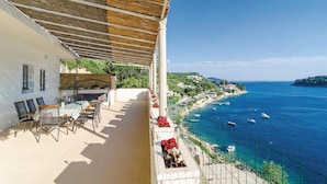 Ein Balkon mit Tisch und Stühlen, mit Blick auf eine Küstenlandschaft mit Booten und freiem Meerblick.