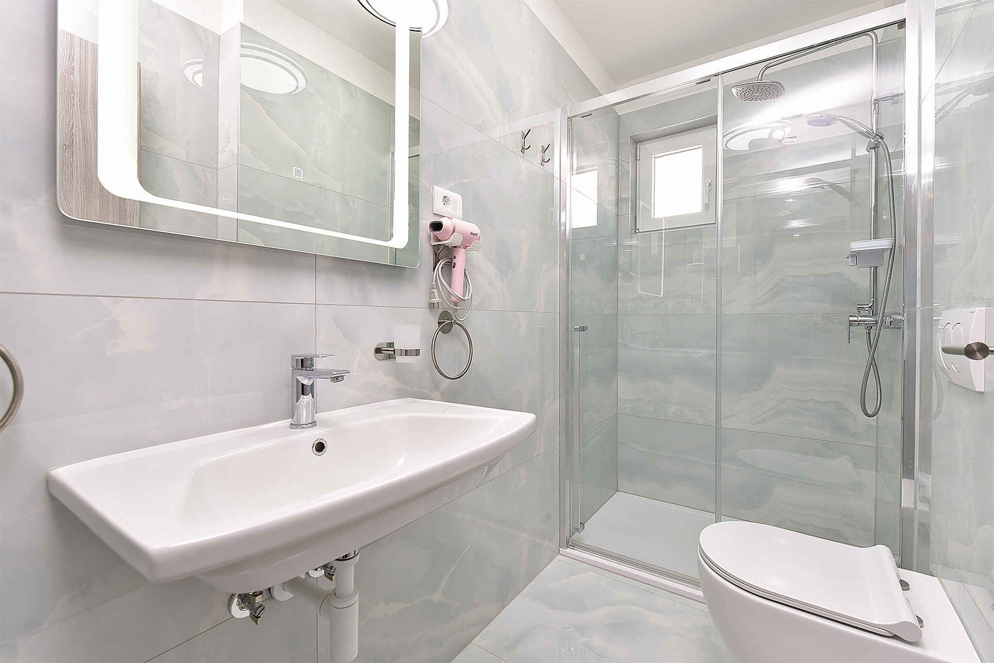 Ein Badezimmer mit weißem Waschbecken, einem Spiegel, einer Duschkabine aus Glas und einer Toilette.