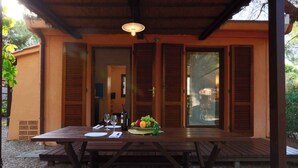 An outdoor wooden table set with a bottle of wine, glasses, and a fruit basket. - Bungalow in a holiday village (Castiglione della Pescaia)