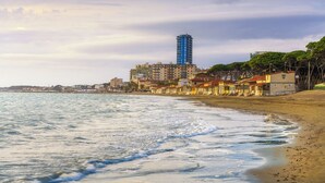 A coastal view with a beach, buildings, and a tall blue structure. - Bungalow in a holiday village (Castiglione della Pescaia)