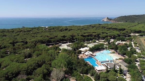 A resort with a large swimming pool surrounded by lush greenery and a view of the sea.