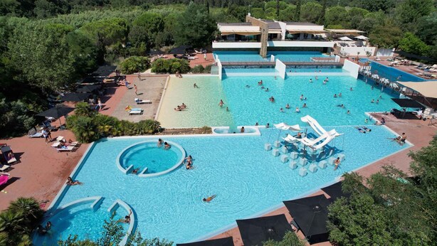 A large outdoor swimming pool with multiple sections, including a central area with a water slide and surrounding smaller pools. - Bungalow in a holiday village (Castiglione della Pescaia)
