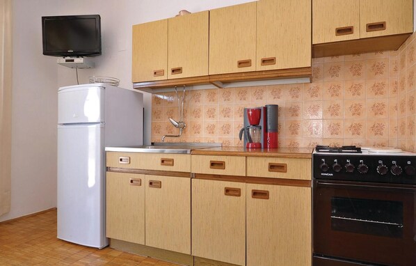 A compact kitchen with wooden cabinets, a white refrigerator, a coffee maker, and a stove. - Nice apartment in Starigrad Paklenica (Starigrad Paklenica)