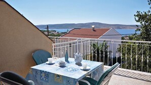 A balcony with a table set for two, overlooking a coastal view with houses and a body of water. - Nice apartment in Starigrad Paklenica (Starigrad Paklenica)