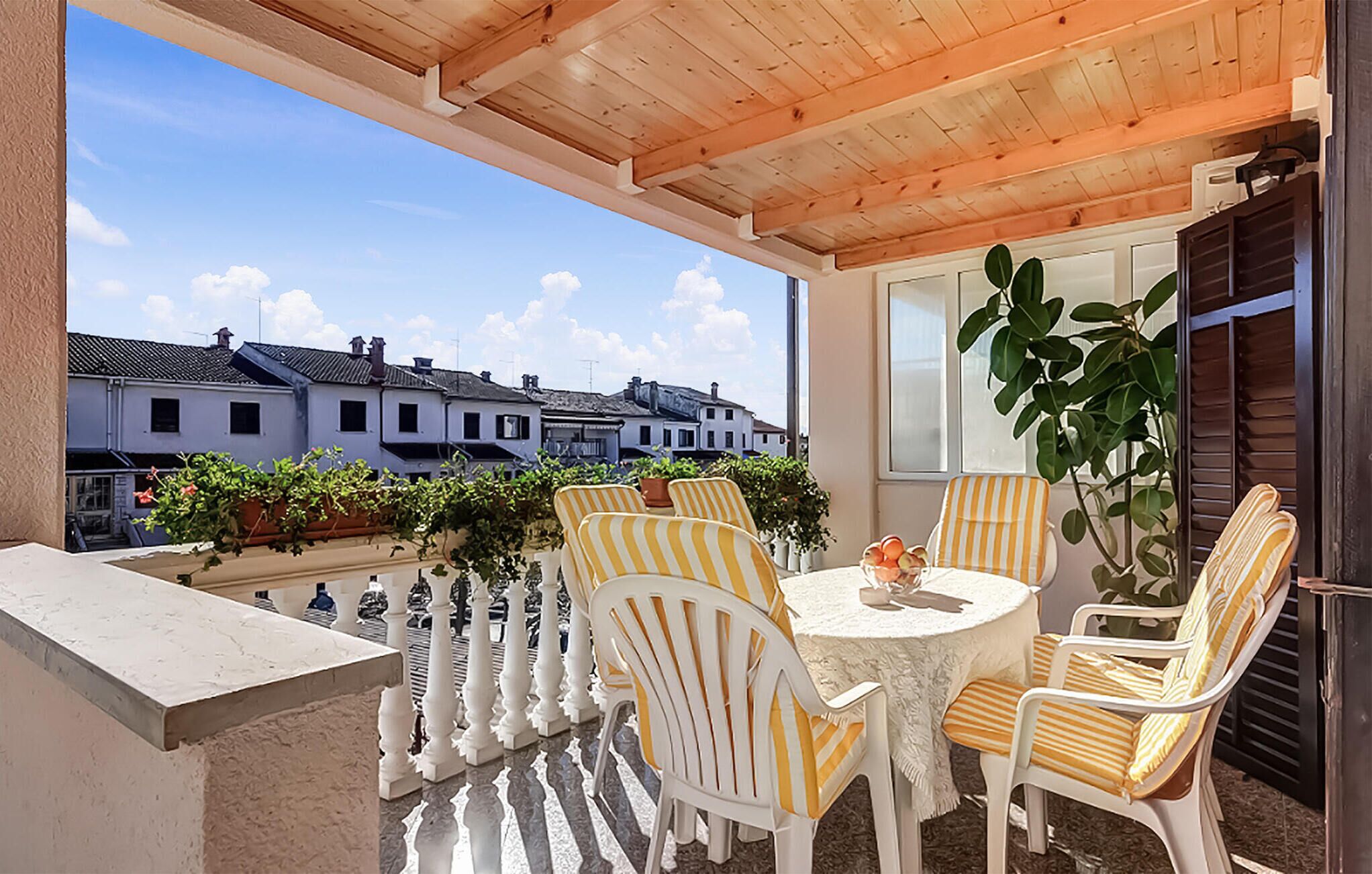 A balcony with white chairs and a table, overlooking a row of white buildings.