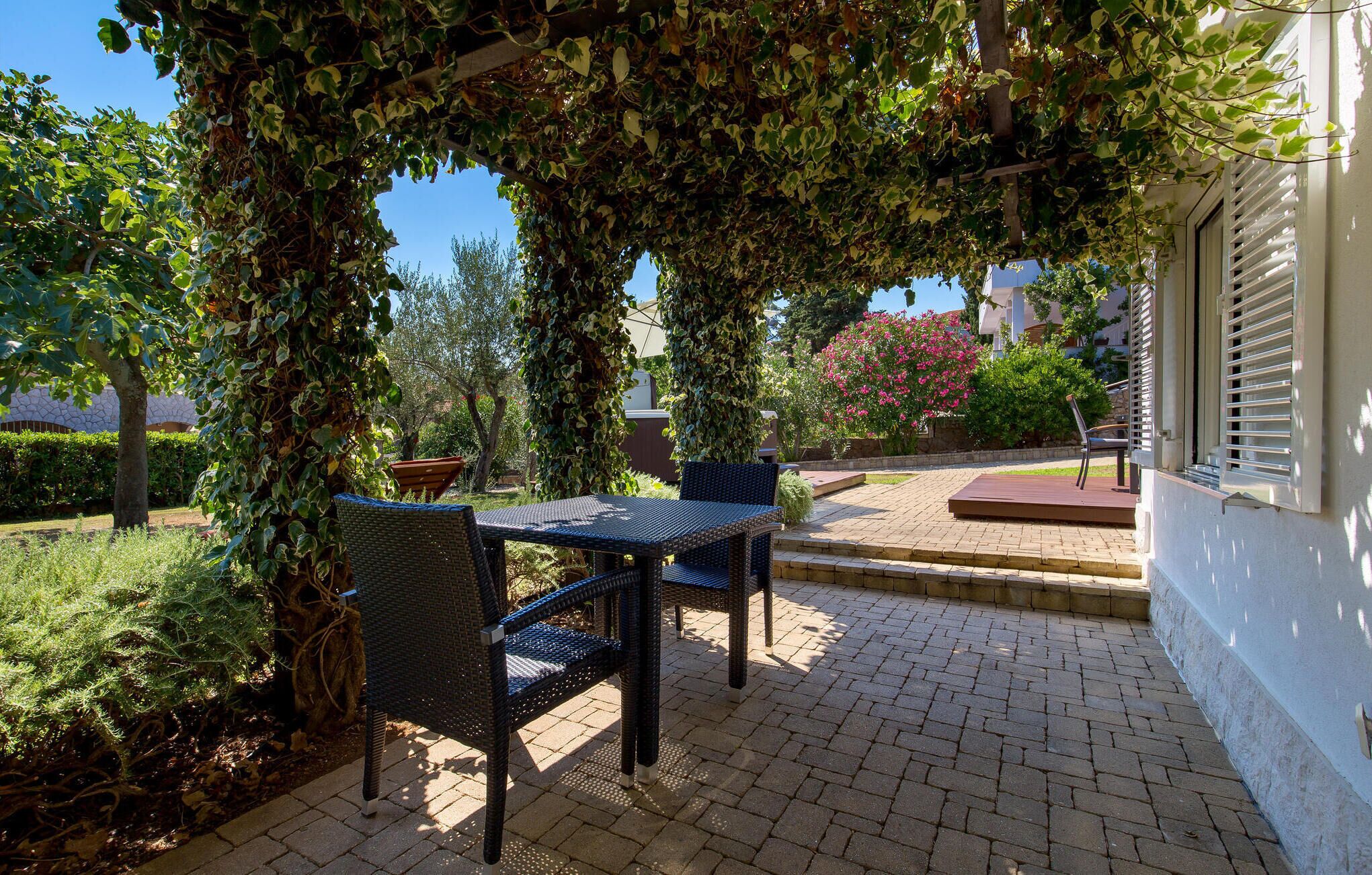 Une terrasse extérieure avec une table et des chaises, entourée d’une végétation luxuriante et dotée d’un sol en briques.