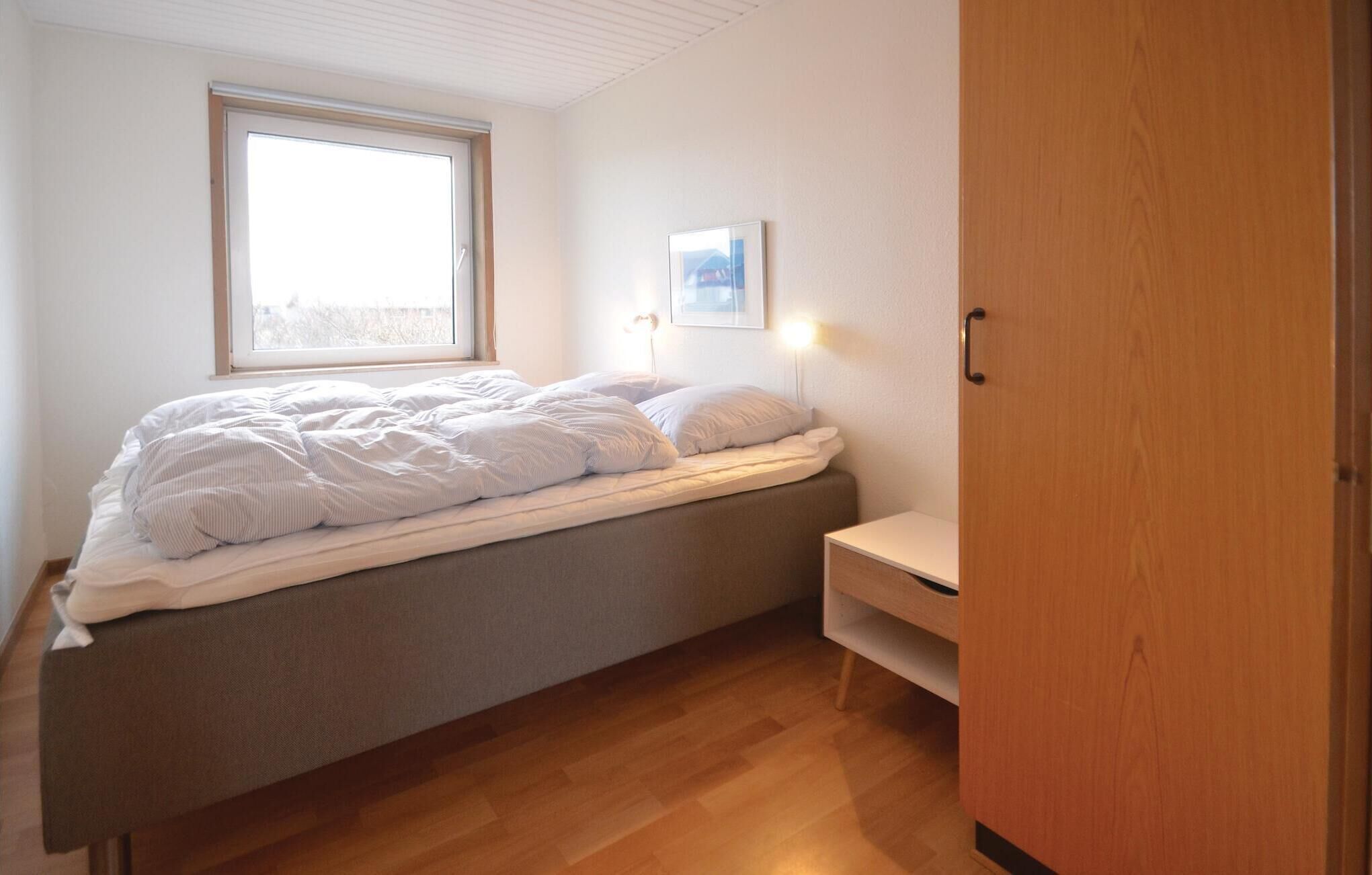 A bedroom with a bed, a window, a wall-mounted picture, and a wooden wardrobe.