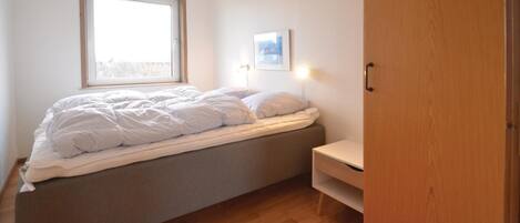 A bedroom with a bed, a window, a wall-mounted picture, and a wooden wardrobe.