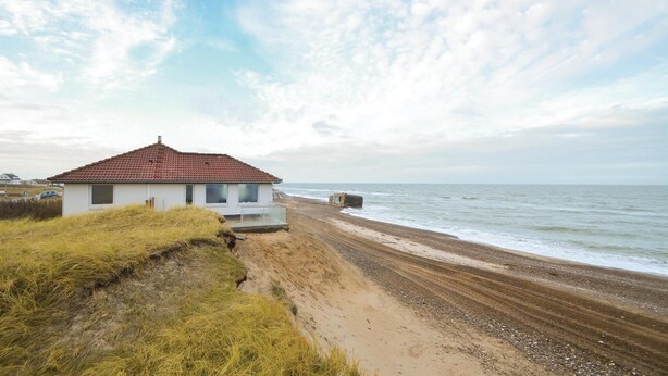 A coastal building with a red-tiled roof, situated on a sandy beach with a view of the sea. - Lovely home in Frøstrup with sauna (Frøstrup)