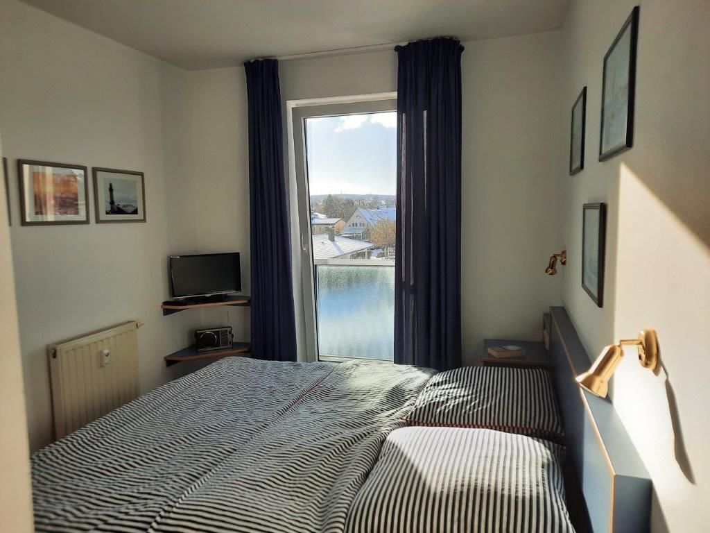 Ein Hotelzimmer mit einem Bett, einem Fernseher, einem Fenster mit Vorhängen und Blick auf Gebäude.