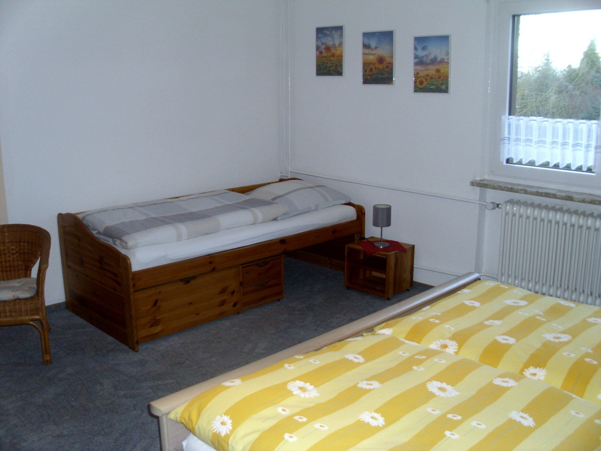 Un dormitorio con una cama individual, una silla, una mesita de noche y tres cuadros en la pared.