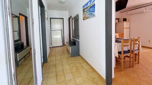 Ein Flur mit Fliesenboden, einem Kühlschrank, einer Mikrowelle und einem Essbereich mit Stühlen und einem Tisch.