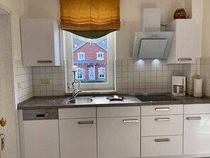 A kitchen with white cabinets, a Siemens dishwasher, a coffee maker, and a window with a view of a red house.