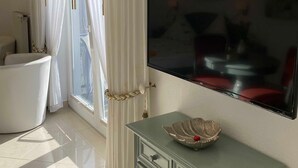 Un salon moderne avec un téléviseur à écran plat fixé au mur, un meuble vert orné d’un vase décoratif et une baignoire blanche.