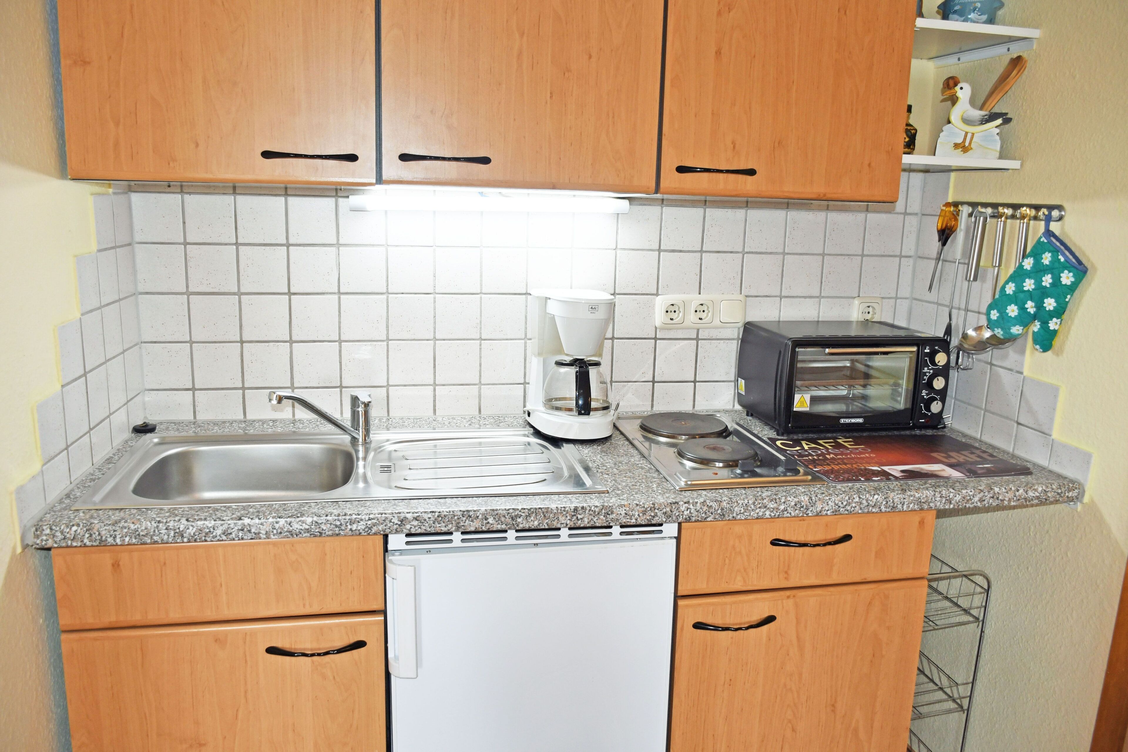 A compact kitchen with wooden cabinets, a built-in dishwasher, a coffee maker, a toaster, and a hanging pot rack.