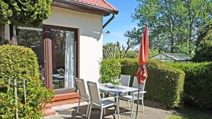 Une terrasse avec une table et des chaises, une porte vitrée et un parasol rouge.