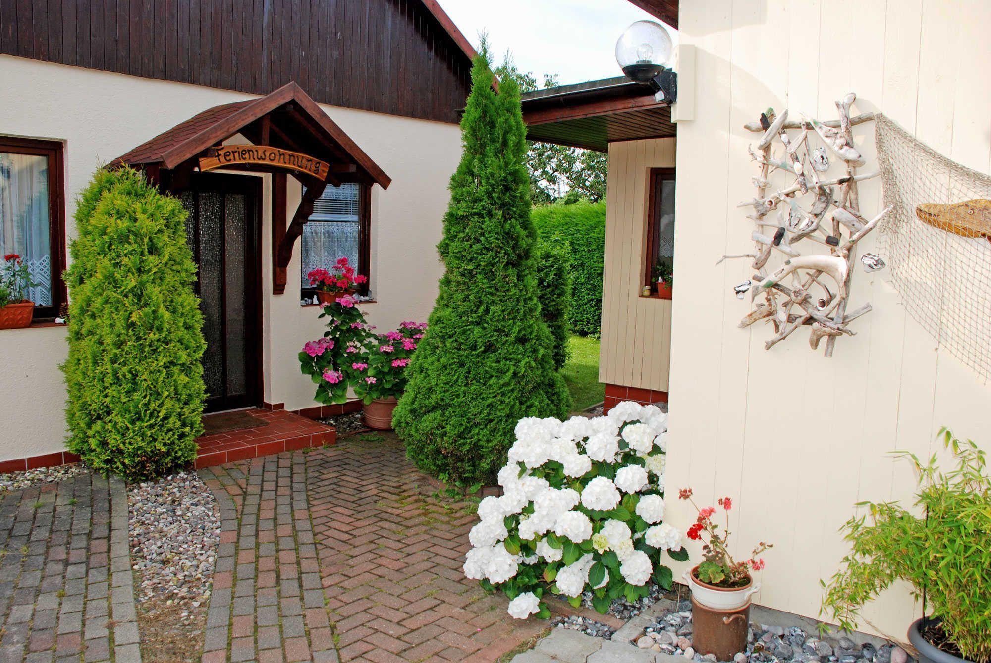 A building with a wooden sign, potted plants, and a wall-mounted bird feeder.
