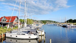 Un port de plaisance où sont amarrés de nombreux voiliers, une maison avec un toit rouge et une eau calme qui reflète les bateaux.
