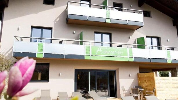 A two-story building with a balcony, a sign reading 'Achenstrasse,' and outdoor seating.