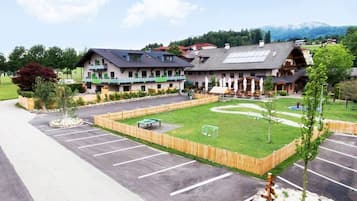 Un hôtel doté d’un parking, d’une pelouse avec un but de football et, en arrière-plan, d’une montagne.
