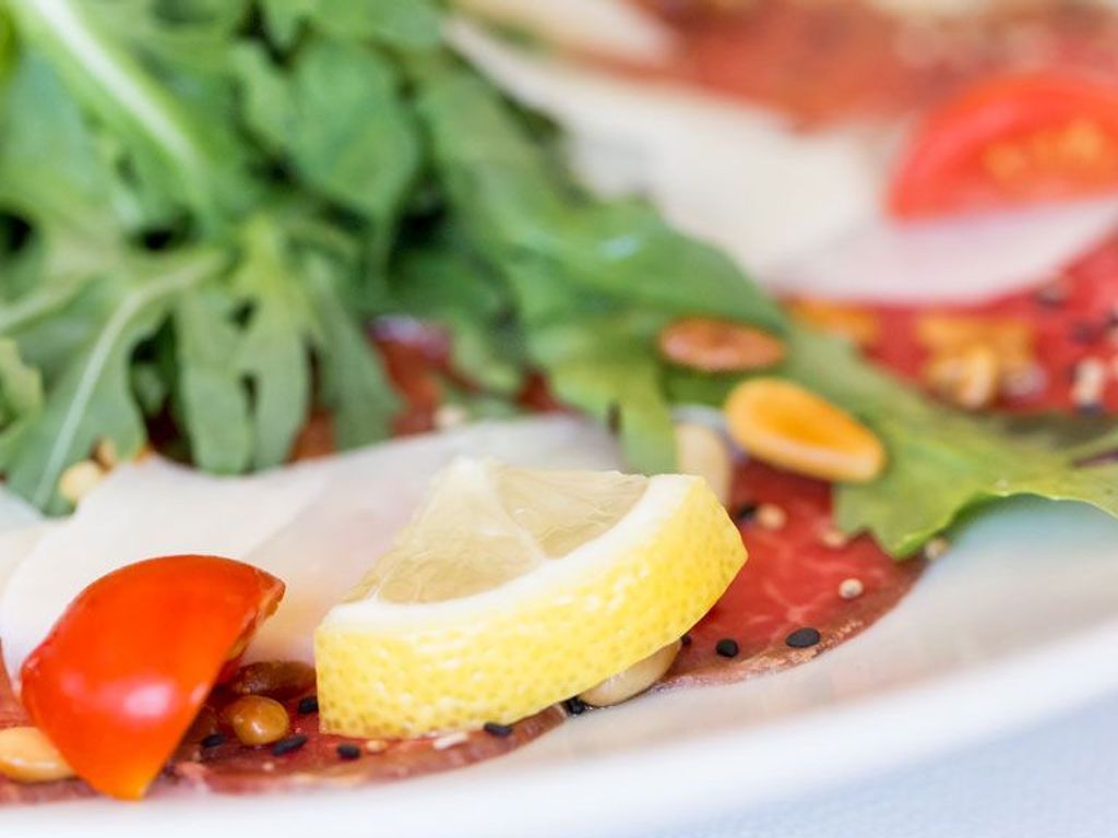A close-up of a dish with greens, a lemon slice, and a red pepper.