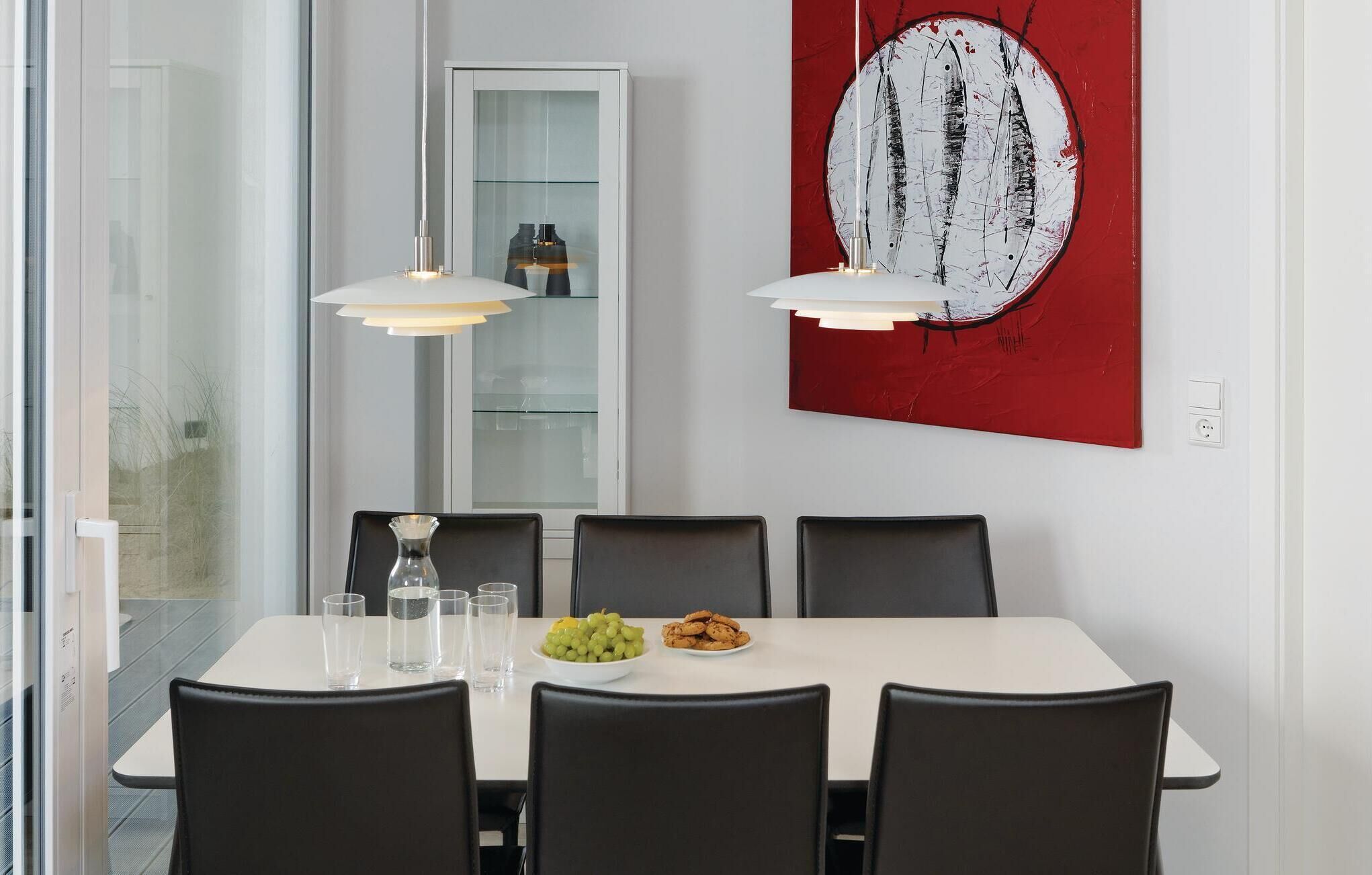 A modern dining area with a white table, black chairs, and a red abstract painting.