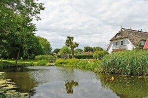A serene riverside scene with a white house with a thatched roof, surrounded by lush greenery and a calm river.