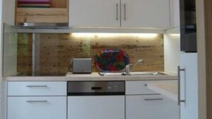 Eine kleine Küche mit weißen Schränken, einem Holzbodenregal, einem Toaster und einem farbenfrohen Geschirrgestell.
