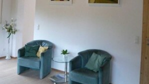 Ein Zimmer mit zwei Sesseln, einem kleinen Tisch und zwei Bildern an der Wand.