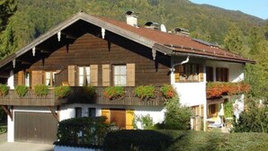 Ein traditionelles Chalet mit geneigtem Dach, Holzfassade und einem Balkon mit Blumentöpfen.