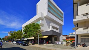 A modern building with a flat facade, large windows, and a parking area in front.