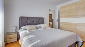 Un dormitori amb un llit, una nitzeta, un armari i una porta que dona a una altra habitació.