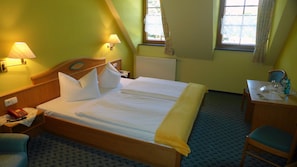 Habitación de hotel con una cama grande, dos lámparas de noche, un escritorio con una silla y una ventana con cortinas.