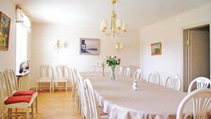Comedor con una larga mesa, sillas blancas, una lámpara de araña y lámparas de pared.