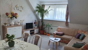 Ein Wohnzimmer mit einer Couch, einem Esstisch mit Stühlen, einem Fernseher und Topfpflanzen.