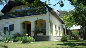 Ein zweistöckiges Haus mit Balkon, überdachter Veranda und einem Garten mit verschiedenen Pflanzen und Blumen.