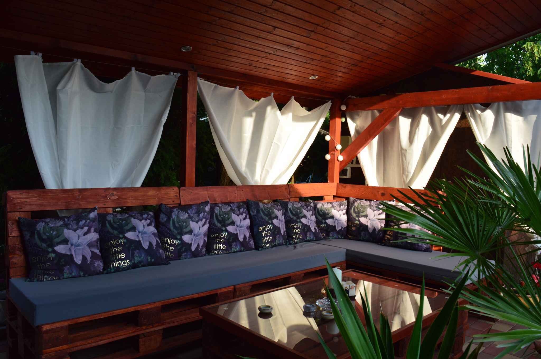 A wooden bench with cushions, a glass table, and white curtains.