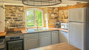 Eine Küche mit einer Steinwand, einem Fenster mit Blick auf Grünflächen, einem Einbauofen, einer Mikrowelle und einem Kühlschrank.